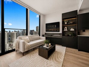A modern living room with a sofa, coffee table, and a city view through large windows.