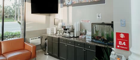 Un hall de hotel con una televisión grande, una estación de café, un sofá y un acuario.