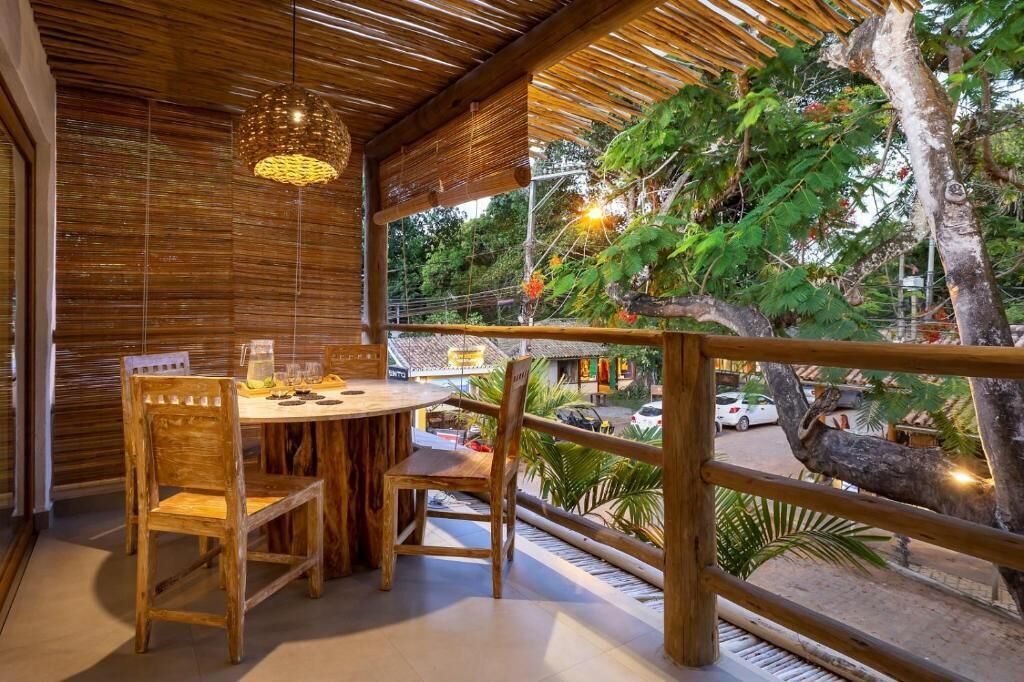 Una mesa de madera con sillas, una lámpara colgante y vista a una calle con coches y árboles.