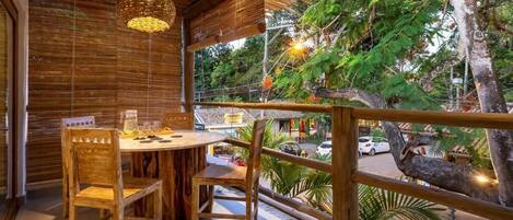 Una mesa de madera con sillas, una lámpara colgante y vista a una calle con coches y árboles.