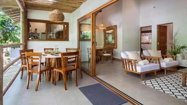 A spacious balcony with wooden furniture, a dining area, and a sliding glass door leading to an interior space. - Flamboyant Residence Quadrado (Porto Seguro)