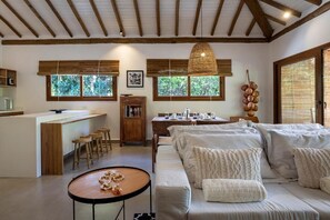 A modern interior with a kitchen, dining area, and living room. There are wooden beams on the ceiling, large windows, and a hanging light fixture. - Flamboyant Residence Quadrado (Porto Seguro)