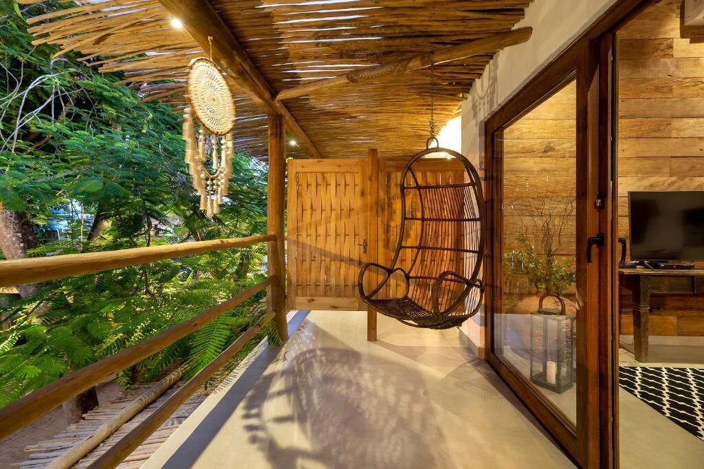 A balcony with a hanging chair, a wooden door, and a television on the right.