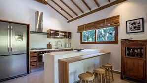 A modern kitchen with a central island, bar stools, a stainless steel refrigerator, and a wooden cabinet. - Flamboyant Residence Quadrado (Porto Seguro)