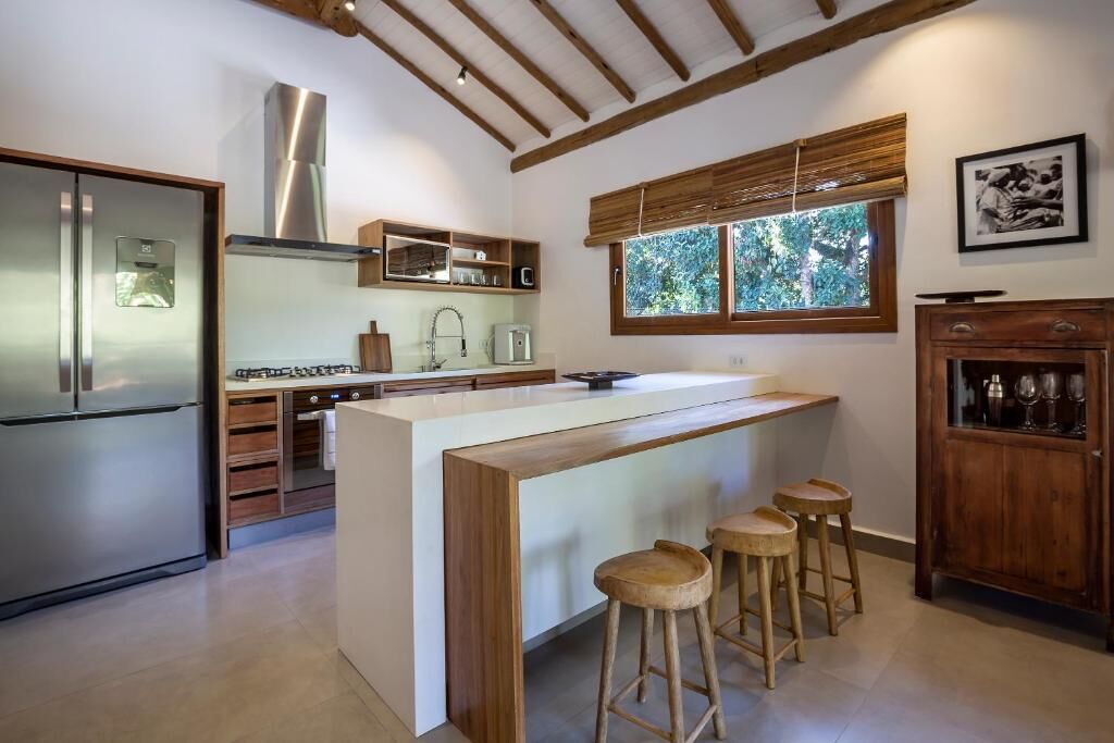 Una cocina moderna con una isla central, taburetes de madera, un refrigerador de acero inoxidable y un ventanal con vistas a zonas verdes.