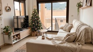 Ein Wohnzimmer mit einer Couch, einem Fernseher, einem Weihnachtsbaum und einem Balkon mit Blick.