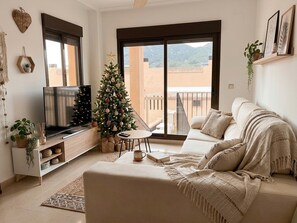 Ein Wohnzimmer mit einer Couch, einem Fernseher, einem Weihnachtsbaum und einem Balkon mit Blick.