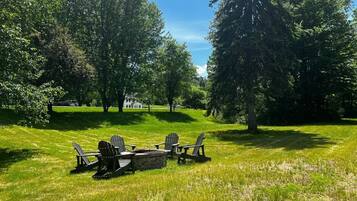 Un espace extérieur verdoyant, agrémenté de fauteuils Adirondack et d’un foyer en pierre.
