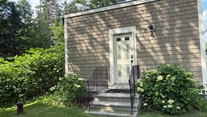 A small, single-story building with a white door and a small porch with steps.