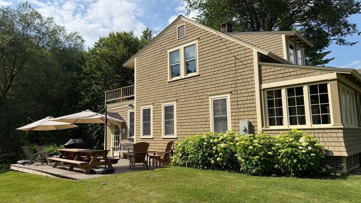A two-story house with a patio area, outdoor seating, and a well-maintained lawn.