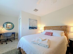 A hotel room with a bed, a desk, a chair, a round mirror, a painting, and a lamp. - BLUE LAGOON (Lauderdale-by-the-Sea)