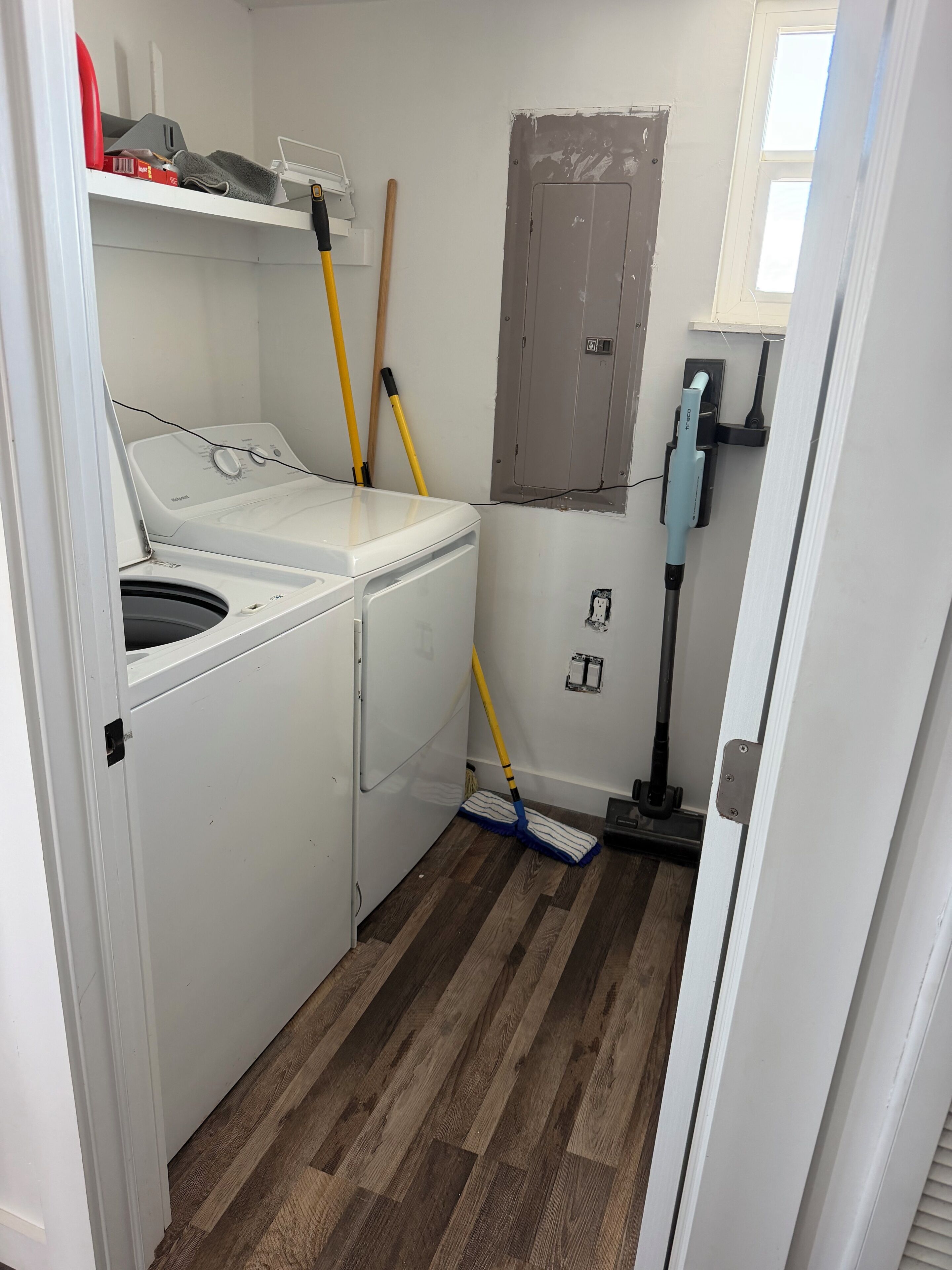 Ein Waschraum mit einer Frontlader-Waschmaschine und einem Trockner, einem Besen, einem Mop und einem Fenster mit Blick.
