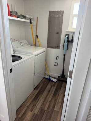 Un cuarto de lavado con lavadora y secadora de carga frontal, un escoba, un trapeador y una ventana con vistas.