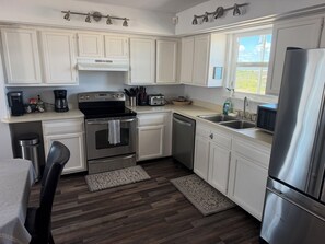 A modern kitchen with white cabinets, stainless steel appliances, and a wooden floor. - Your perfect beach getaway is waiting! 3 bedroom 2 1/2 bathroom beach house. (St. Augustine)
