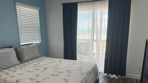 A bedroom with a bed, a window with blinds, a balcony with a chair, and a view of the outdoors. - Your perfect beach getaway is waiting! 3 bedroom 2 1/2 bathroom beach house. (St. Augustine)
