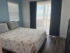 A bedroom with a bed, a window with blinds, a balcony with a chair, and a view of the outdoors. - Your perfect beach getaway is waiting! 3 bedroom 2 1/2 bathroom beach house. (St. Augustine)