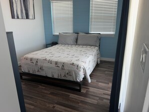 A bedroom with a bed, two bedside tables, and a window with blinds. - Your perfect beach getaway is waiting! 3 bedroom 2 1/2 bathroom beach house. (St. Augustine)