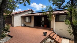 Ein Wohnhaus mit einer Holterrasse, einer überdachten Terrasse und einem kleinen Gartenbereich mit Topfpflanzen.