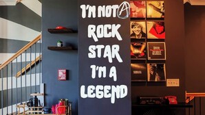 Um quarto com uma escada, uma parede com cartazes emoldurados de bandas de rock e um pilar preto com texto branco.