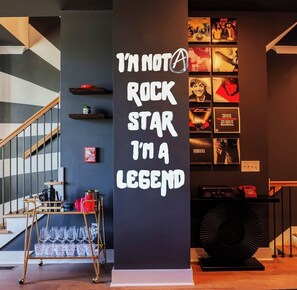 A room with a staircase, a wall with framed rock band posters, and a black column with white text. - Nashville Legendz: Rooftop Deck (Nashville)