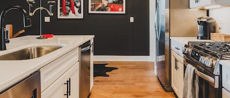 Una cocina moderna con electrodomésticos de acero inoxidable, piso de madera y un tapete con estampado rojo y blanco.