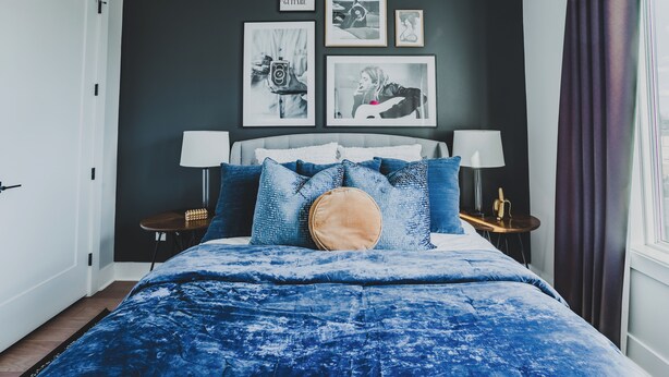 Quarto com cama, almofadas, mesa de cabeceira, abajur e obras de arte na parede.