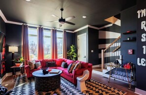 A modern living room with a red sofa, a round coffee table, and a ceiling fan. - Nashville Legendz: Rooftop Deck (Nashville)