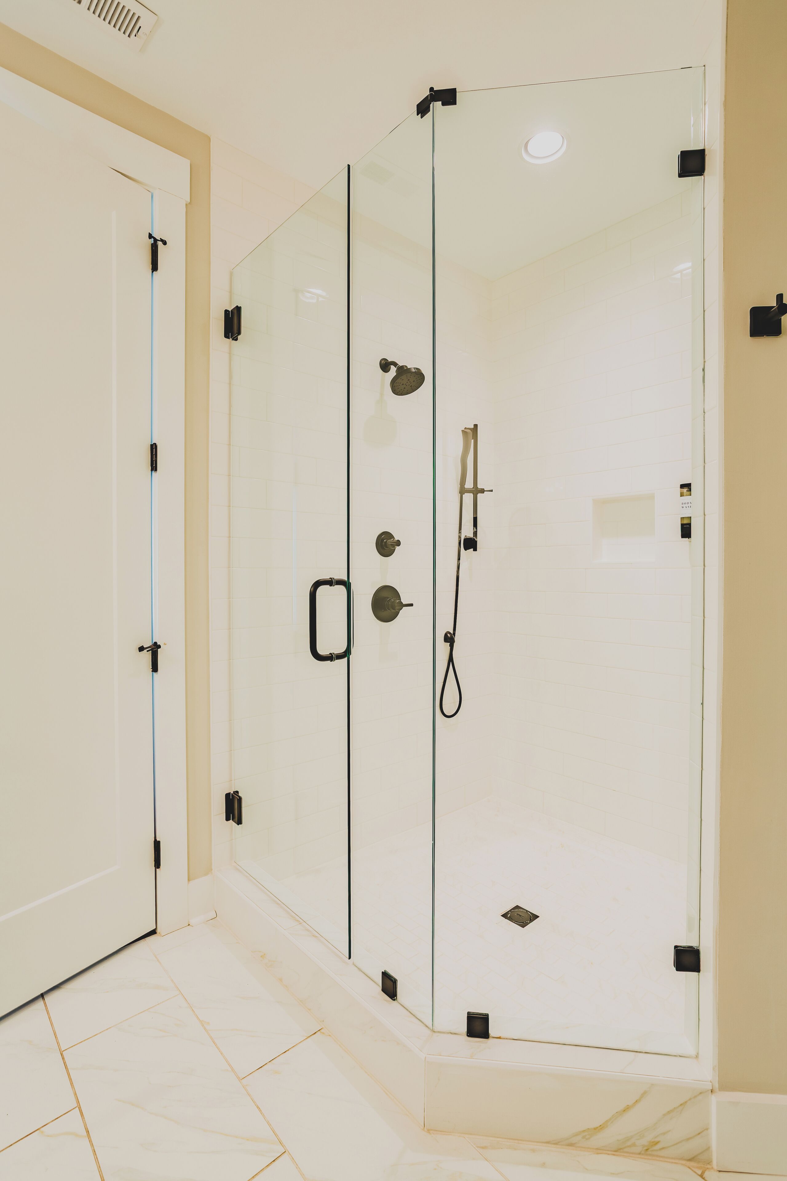 A glass-enclosed shower with a handheld showerhead and a handheld faucet.