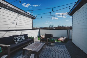 An outdoor patio with a sofa, chairs, a table, and string lights. - Nashville Legendz: Rooftop Deck (Nashville)