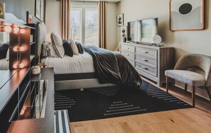 Ein modernes Schlafzimmer mit Bett, Kommode, Schminktisch mit Beleuchtung und Fernseher.