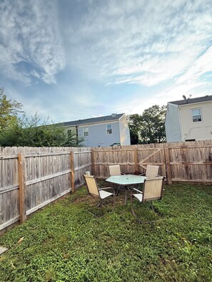 A backyard with a wooden fence, a metal table, and four chairs. - Lake Access 3 Bedroom Townhome Near Chic's Beach & Airport (Virginia Beach)