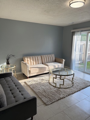 A living room with a beige sectional sofa, a dark grey sofa, a glass coffee table, and a small side table with a plant. - Lake Access 3 Bedroom Townhome Near Chic's Beach & Airport (Virginia Beach)