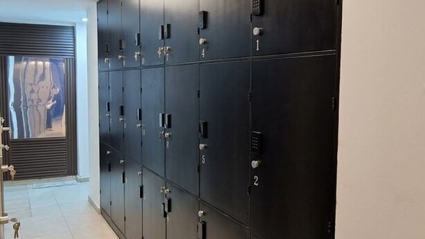A row of dark-colored lockers with numbered compartments, a tiled floor, and a door with a metal handle. - Capsule (Mexico City)