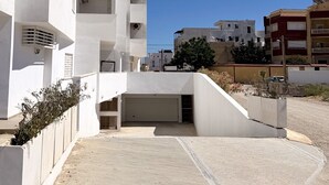 A modern white building with multiple balconies and a covered parking area.