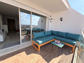 Un balcón con suelo de madera, un sofá color turquesa y una mesita con un objeto decorativo.