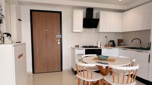 A modern kitchen with white cabinetry, a wooden door, a round dining table with chairs, and a woven mat on the floor.