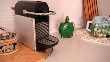 Een keuken met een koffiezetapparaat, een groene decoratieve fles en een klein modelhuis.