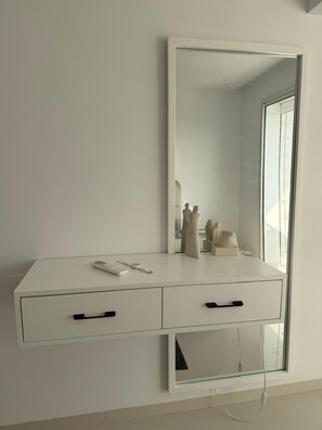 Un tocador blanco con un espejo grande, dos cajones y un pequeño estante decorado con adornos.