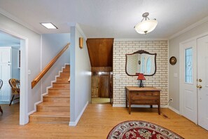 A staircase leading to a second floor, a wooden cabinet with drawers, a mirror on the wall, and a patterned rug on the floor.
