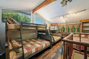 Ein Schlafsaalzimmer mit Etagenbetten, einem Holztisch und einem Fenster mit Vorhängen.