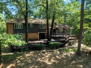 A two-story cabin with a deck and a covered outdoor seating area, surrounded by trees. - Hilltop Lodge -  27 Guests, 5 bedroom + loft beds (Broken Bow)