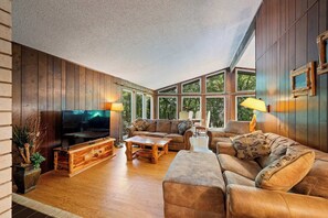 A cozy living room with wooden walls, a large TV, and comfortable seating.