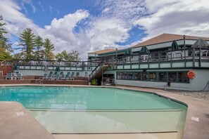A swimming pool with a deck area, lounge chairs, and a building with a balcony. - The Summit House at Waterville Estates w/Amenities (Campton)