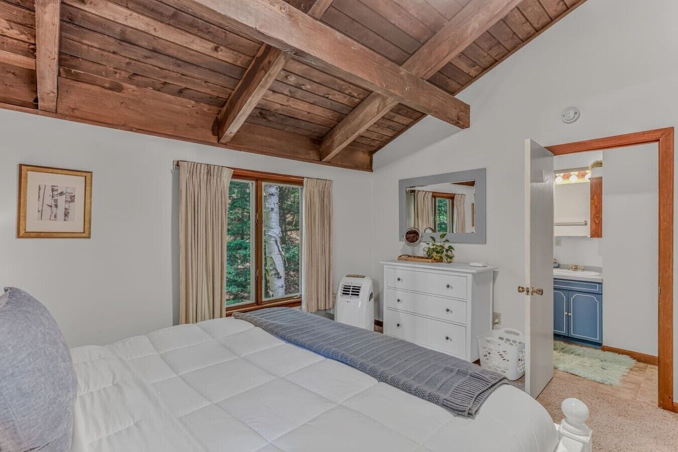 A bedroom with a bed, a dresser, a mirror, and a window with curtains.