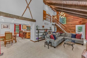A spacious living area with a large sofa, a dining table with chairs, a staircase, and a bookshelf. - The Summit House at Waterville Estates w/Amenities (Campton)