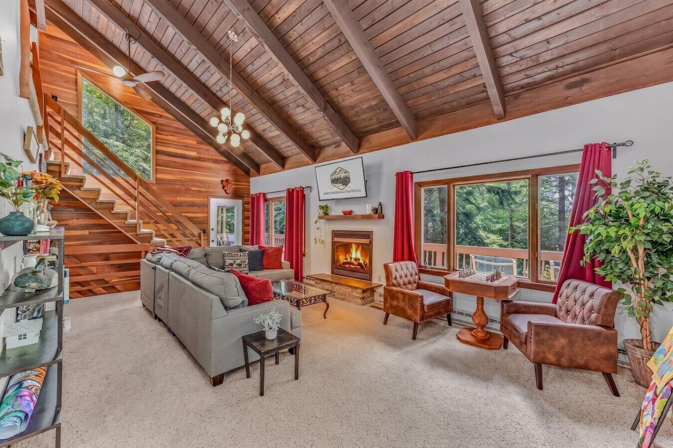 A cozy living room with a fireplace, a staircase, and large windows.