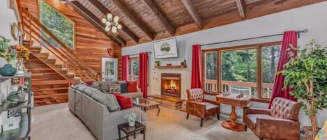 A cozy living room with a fireplace, a staircase, and large windows.