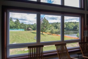 Ein Zimmer mit großen Fenstern und Blick auf eine Rasenfläche, eine kleine Bebauung und ein Gewässer.