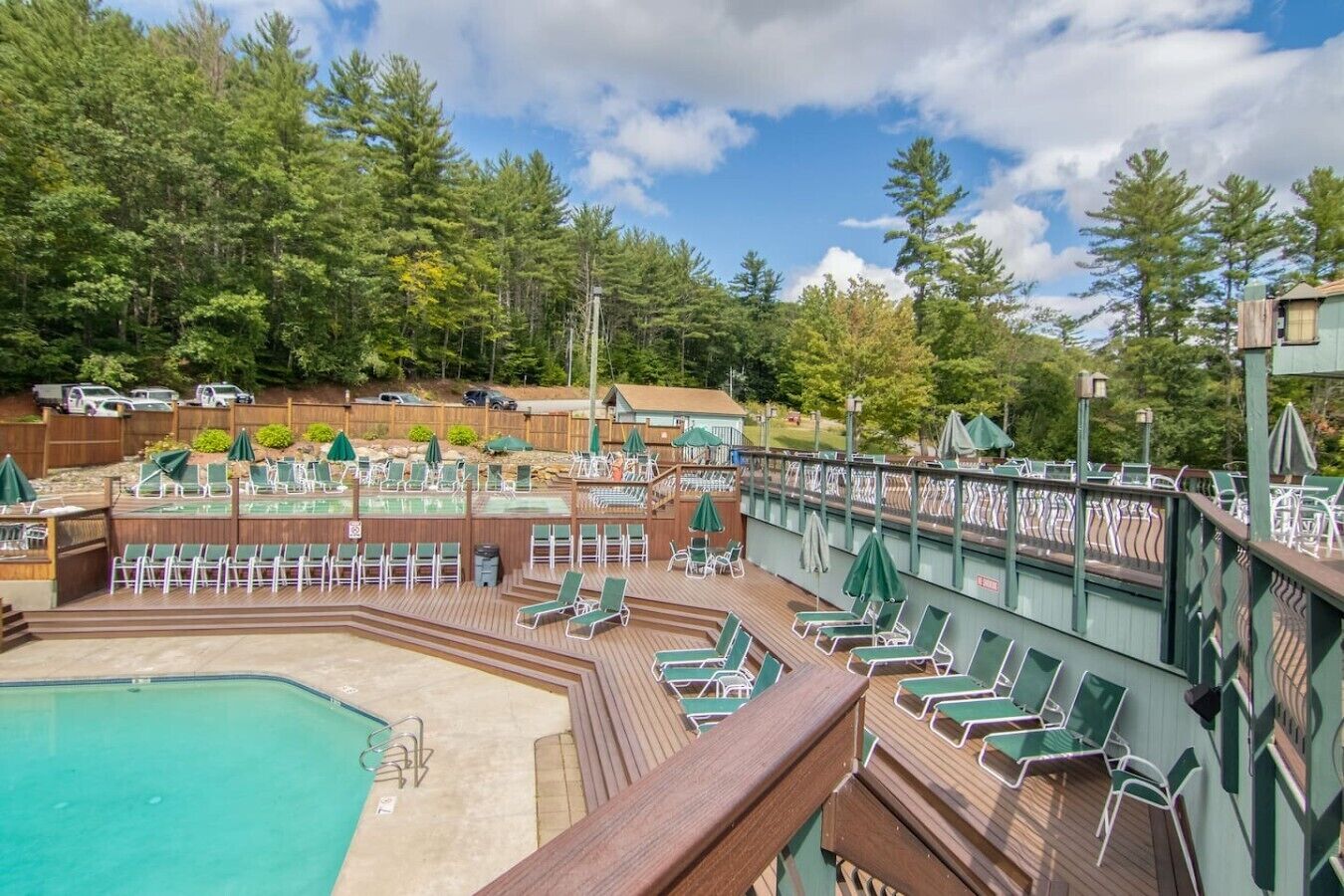 Un espace piscine doté de plusieurs niveaux de chaises longues et de parasols, entouré d’une terrasse en bois et d’une clôture en bois.