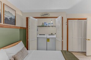 A bedroom with a bed, a laundry area with a sign, and a closet with louvered doors. - The Summit House at Waterville Estates w/Amenities (Campton)